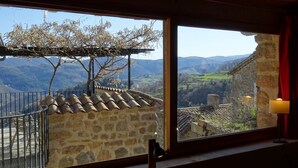 A room with a large window overlooking a mountainous landscape, stone walls, and a tiled roof. - Gite de Chapelèche les Glycines Pour 8 à 10 Personnes (Gluiras)