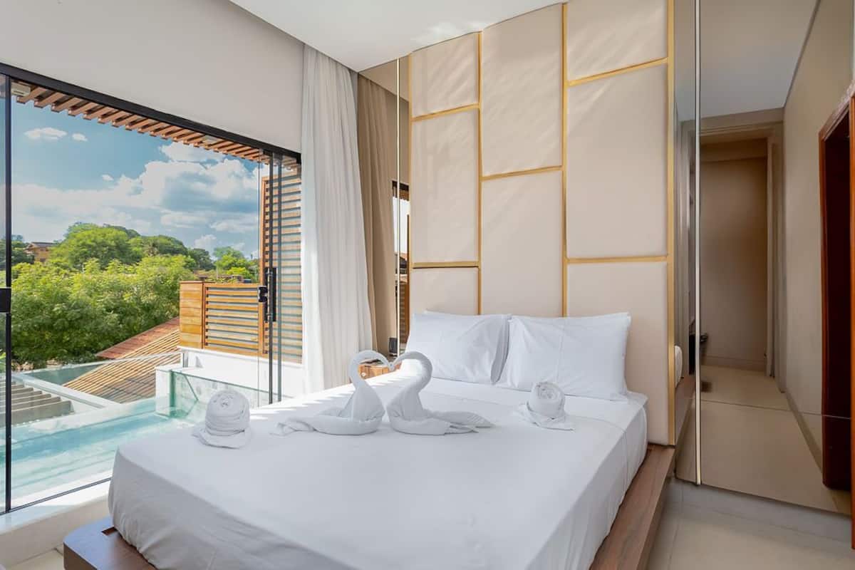 Ein Hotelzimmer mit einem großen Bett, Blick auf Grünflächen und einem Pool im Freien sowie einer Schiebetür zu einem weiteren Raum.