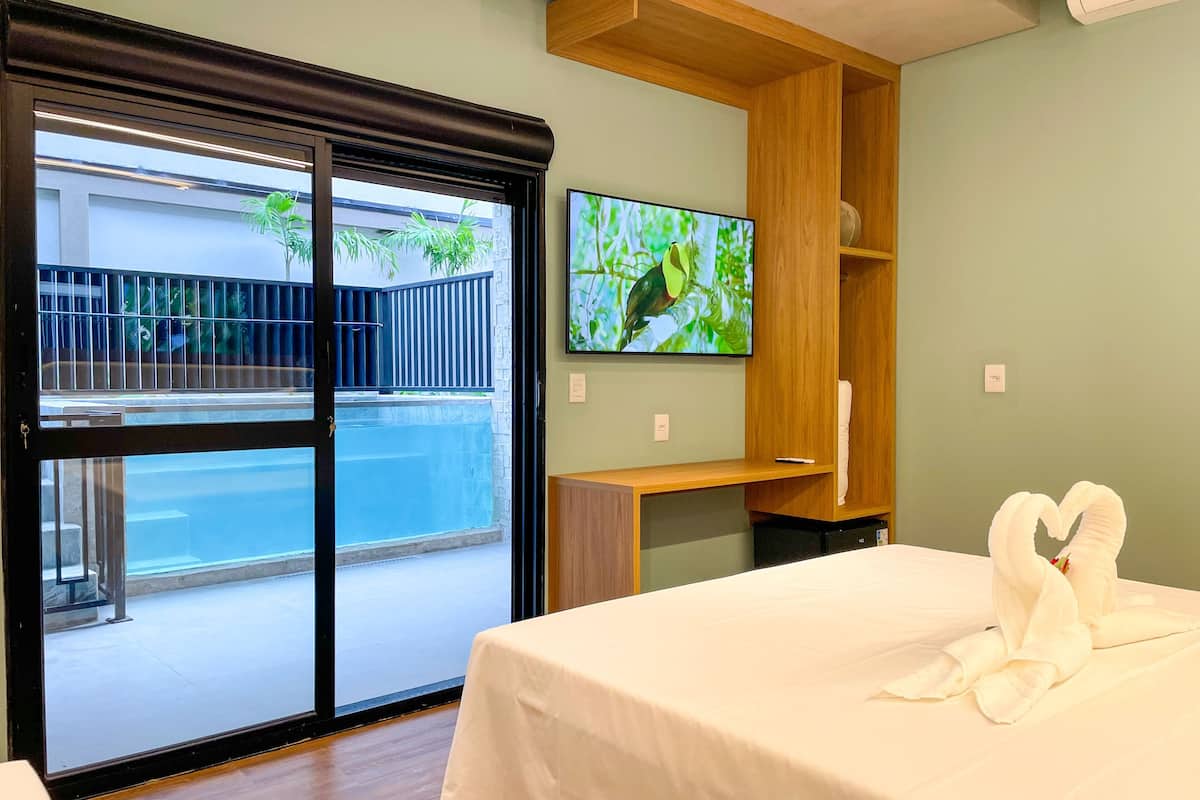 Ein Hotelzimmer mit einem Bett, einem Fernseher, einem Holztisch und Blick auf einen Pool.