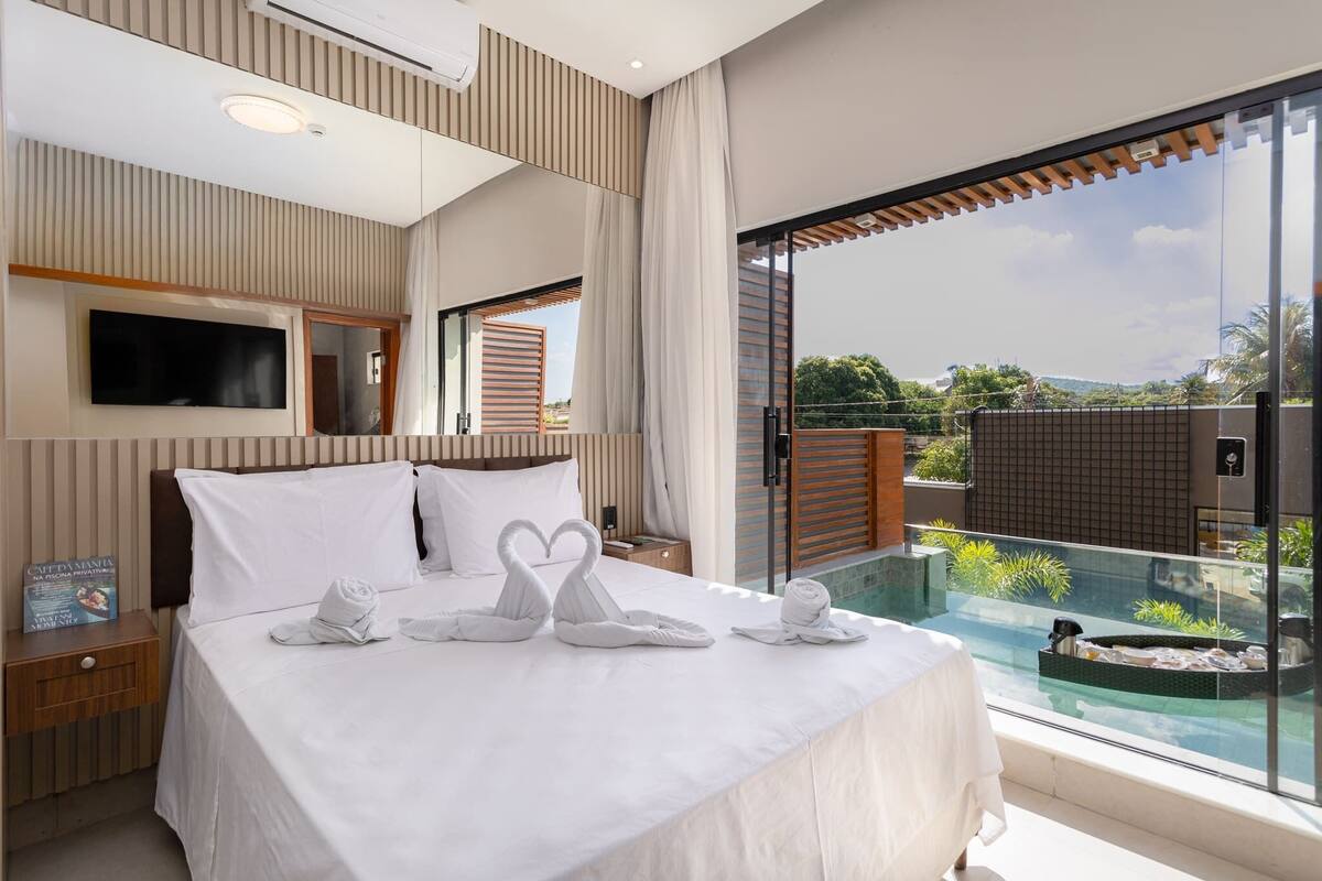 Ein modernes Hotelzimmer mit einem großen Bett, einem an der Wand befestigten Fernseher und einem Balkon mit Pool.