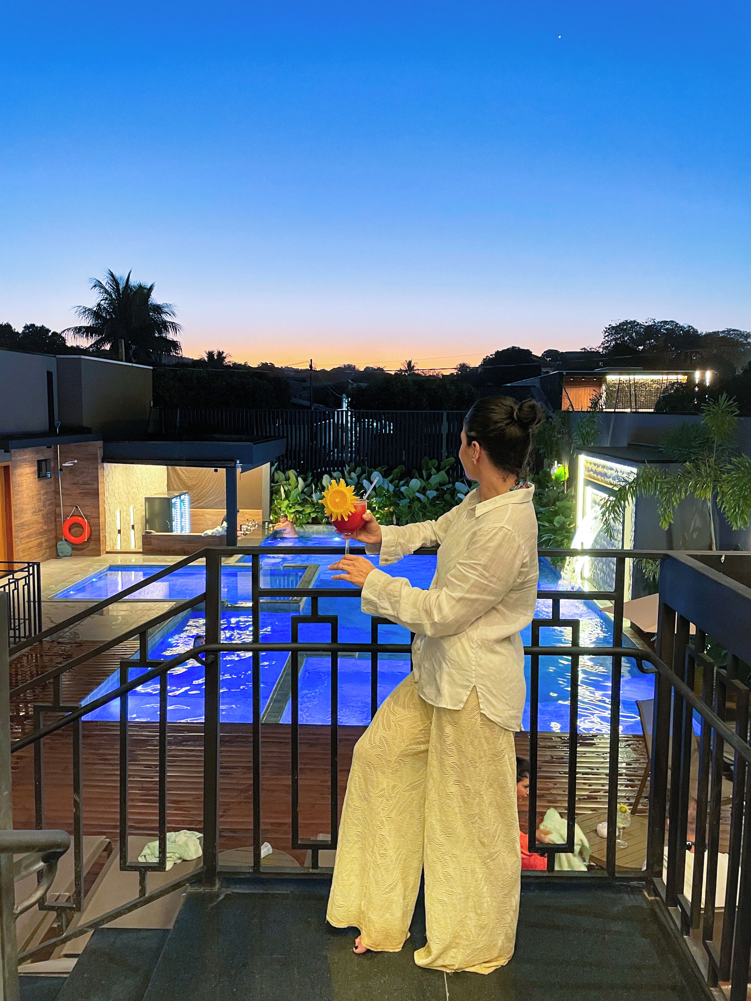 A person holding a flower near a pool with a view of a building and a fence.