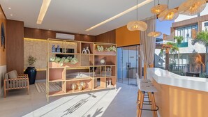 A modern hotel lobby with a reception desk, wooden shelving with decorative items, a seating area, and a view of the outside.