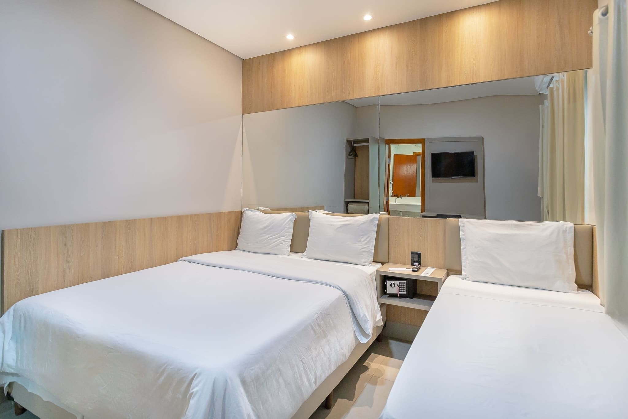 Een hotelkamer met twee bedden, een televisie, een spiegel en een nachtkastje met een telefoon.