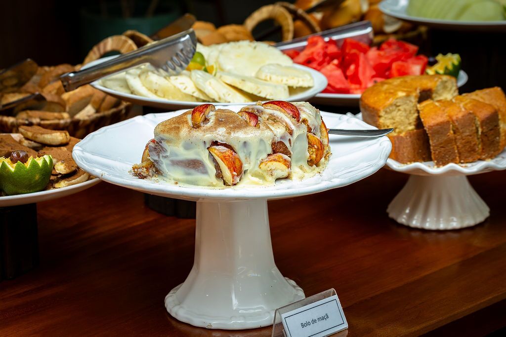 A buffet with various dishes including a cake labeled "Bolo de maçã" and other food items.