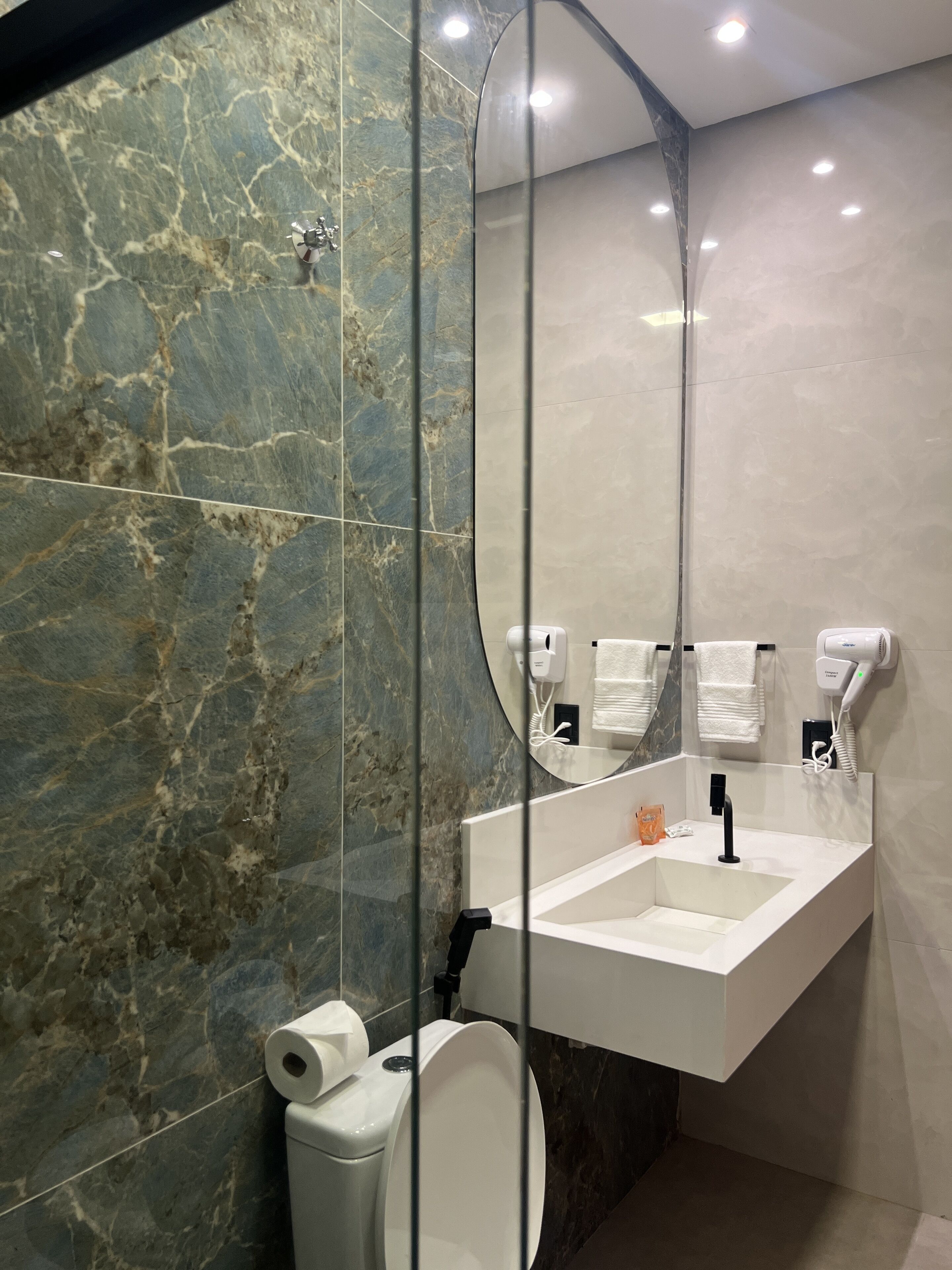 Une salle de bain moderne avec un mur en marbre, une cloison en verre, un lavabo, des toilettes et un miroir.