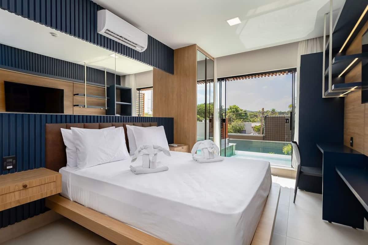 Ein modernes Schlafzimmer mit einem großen Bett, einem Schreibtisch und Blick auf einen Swimmingpool.