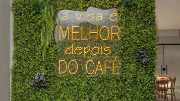 A wall with a green leafy texture and a sign that reads "a vida é melhor depois do café".