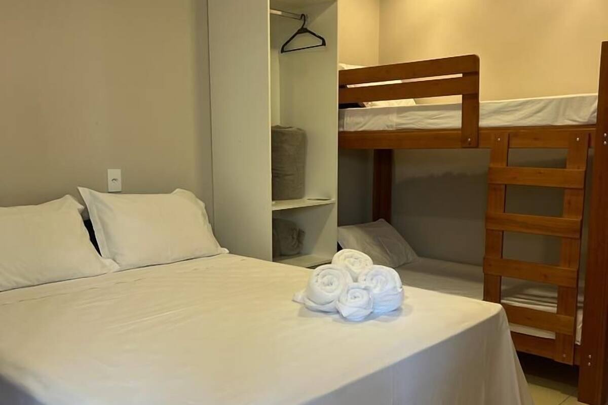 Ein Zimmer mit einem Einzelbett, einem Stockbett, einem Kleiderschrank und einem ordentlich bezogenen Bett mit Handtüchern.