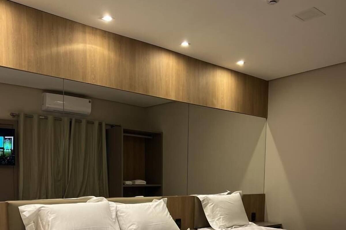 Ein modernes Hotelzimmer mit einem großen Bett, einem Nachttisch, einem Kleiderschrank und einem großen Spiegel.