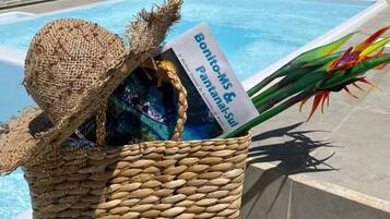 Una cesta de mimbre con un sombrero, un folleto y flores coloridas junto a una piscina.