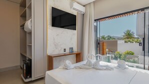 A modern hotel room with a bed, a TV, a minibar, and a view of the outdoors.