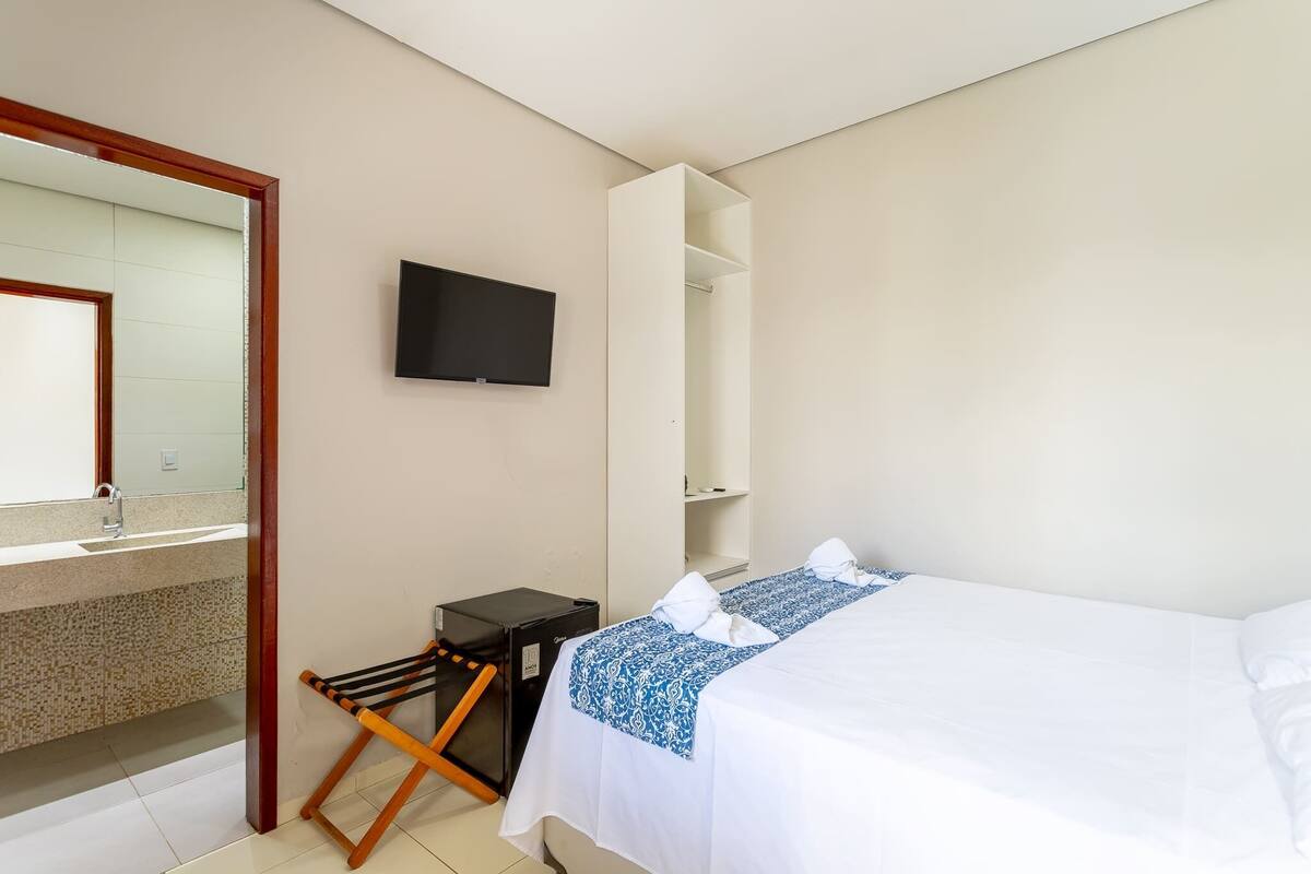 Ein Hotelzimmer mit einem Bett, einem Fernseher, einem kleinen Schreibtisch und einem durch eine geöffnete Tür einsehbaren Badezimmer.