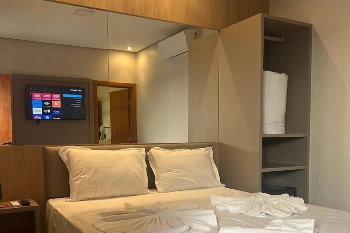 Ein modernes Hotelzimmer mit einem großen Bett, einem flachbildfernseher an der Wand und einem eingebauten Kleiderschrank.