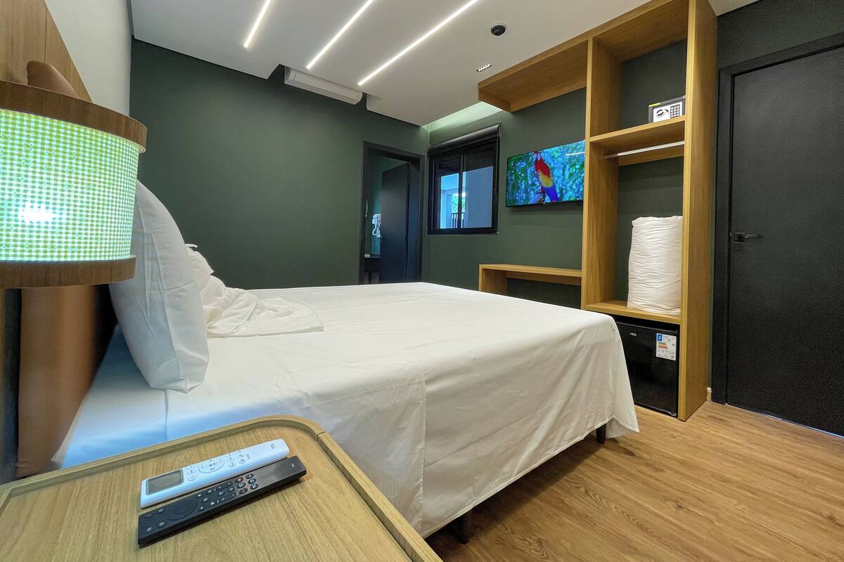 Ein modernes Hotelzimmer mit Bett, Nachttischlampe, Fernseher und Ablagefläche mit Handtüchern.