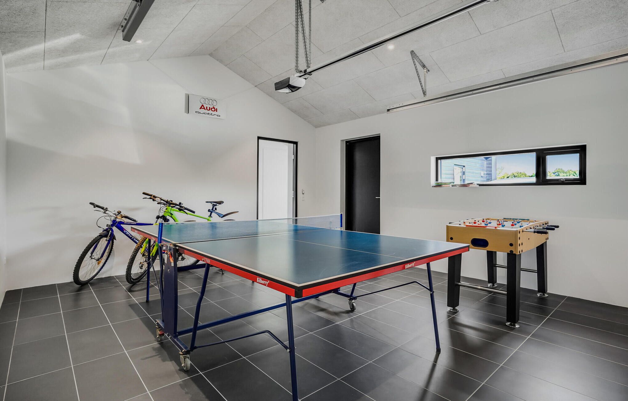 A room with a ping pong table, bicycles, and a foosball table.