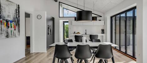A modern kitchen with a dining area, featuring a large window, a hanging light fixture, and a clock on the wall.