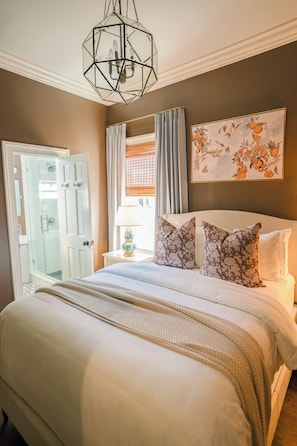 Ein Schlafzimmer mit einem großen Bett, einem geometrischen Kronleuchter, einer Duschkabine und einem Gemälde von Orangen.