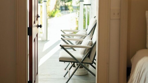 An open door leading to a porch with a wooden floor and a row of white lounge chairs.
