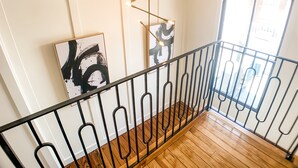 Una escalera con piso de madera y barandilla de metal negro que lleva a un balcón con vistas a edificios.
