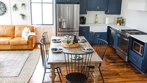 A modern kitchen with dark blue cabinets, a wooden dining table, and a leather sofa. - Guesthouse Charleston: EAST (46 H) (Charleston)
