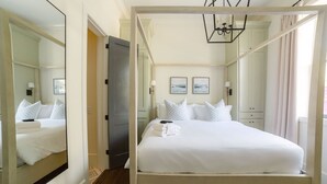 Een hemelbed met witte lakens, een spiegel aan de muur en twee ingelijste foto's.