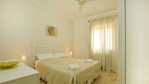 A bedroom with a bed, a bedside table, a ceiling fan, and a window with curtains. - Awesome apartment in Contrada Fiori Sud (Contrada Fiori Sud)