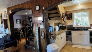 Un interior rústico con un piano, una escalera, una zona de cocina y un ventanal grande.