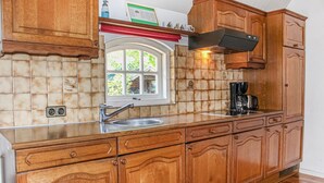 A kitchen with wooden cabinets, a stainless steel sink, and a window with a view of greenery outside. - 1 bedroom cozy home in Udenhout (Udenhout)