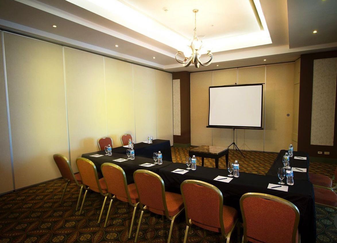 A conference room with a long table, chairs, a projector screen, and a chandelier.