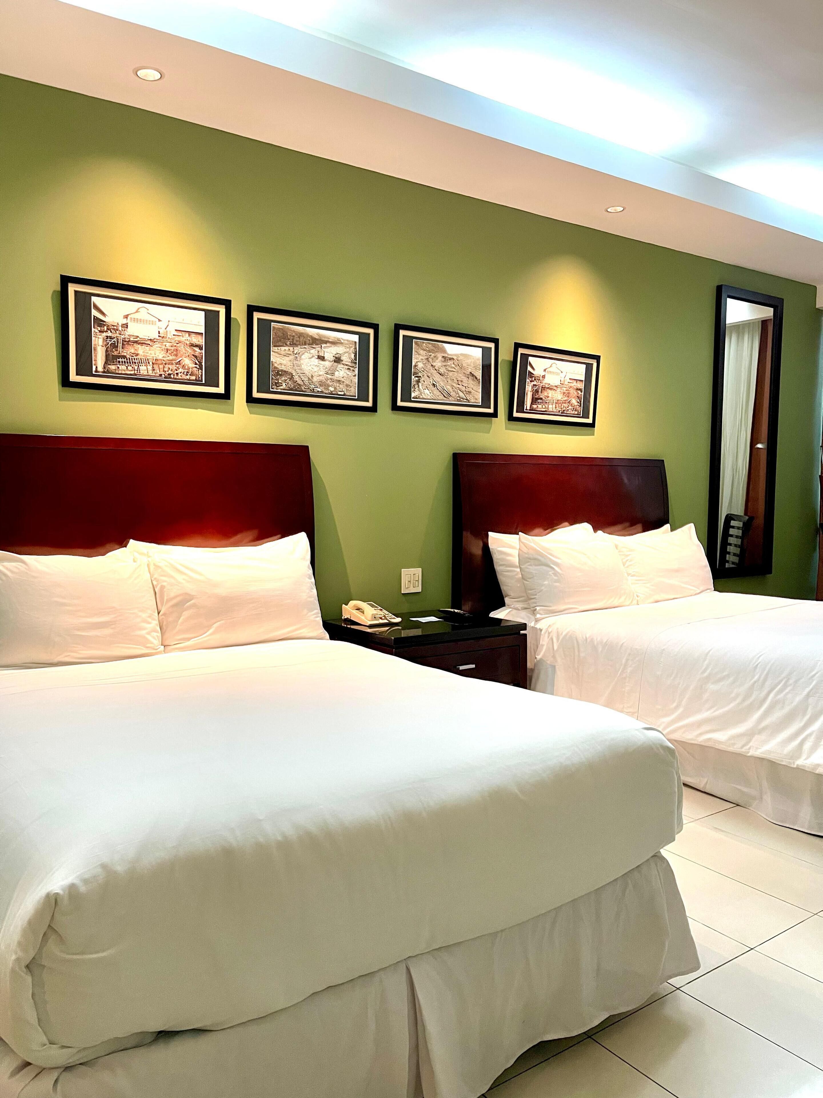 Habitación de hotel con dos camas, paredes verdes y cuadros en la pared.