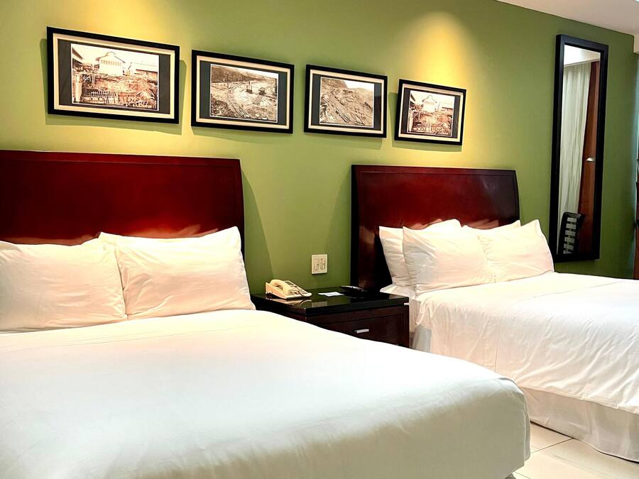 Habitación de hotel con dos camas, paredes verdes y cuadros en la pared.