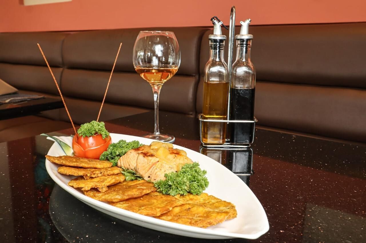 A dining table with a plate of food, a glass of wine, and two bottles of sauce.