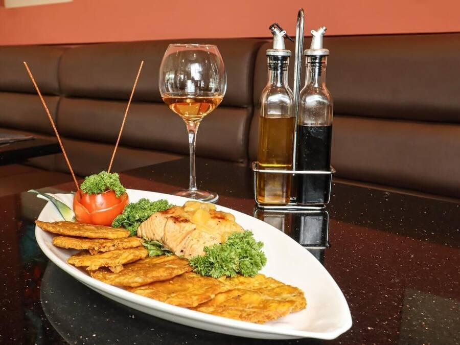 A dining table with a plate of food, a glass of wine, and two bottles of sauce.