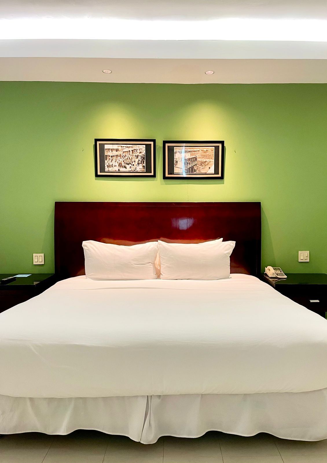 Una habitación de hotel con una cama grande, paredes verdes y dos cuadros enmarcados.