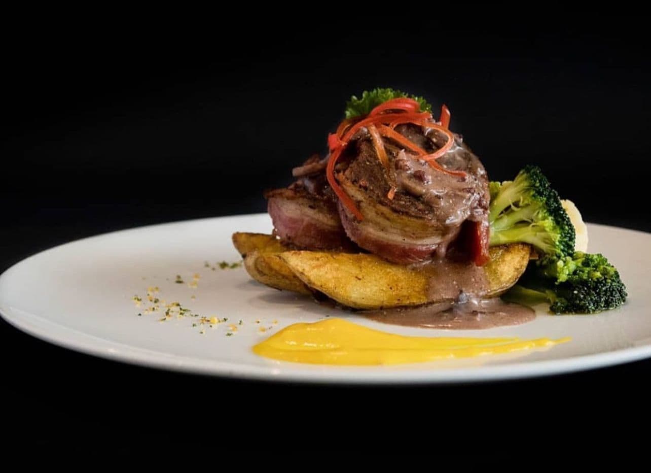Un plato con un filete cubierto de salsa roja y verduras, acompañado de papas y brócoli.