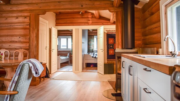A log cabin interior with a wooden dining table, chairs, a kitchen with a sink, and a fireplace. - Nice home in Kvam with kitchen (Kvam)