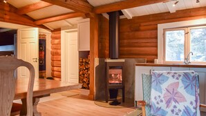A cozy cabin interior with a wood-burning stove, a dining table, and a window with a view. - Nice home in Kvam with kitchen (Kvam)
