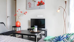 Un soggiorno moderno con una televisione, un vaso con fiori rossi e un quadro raffigurante fiori rossi appeso al muro.