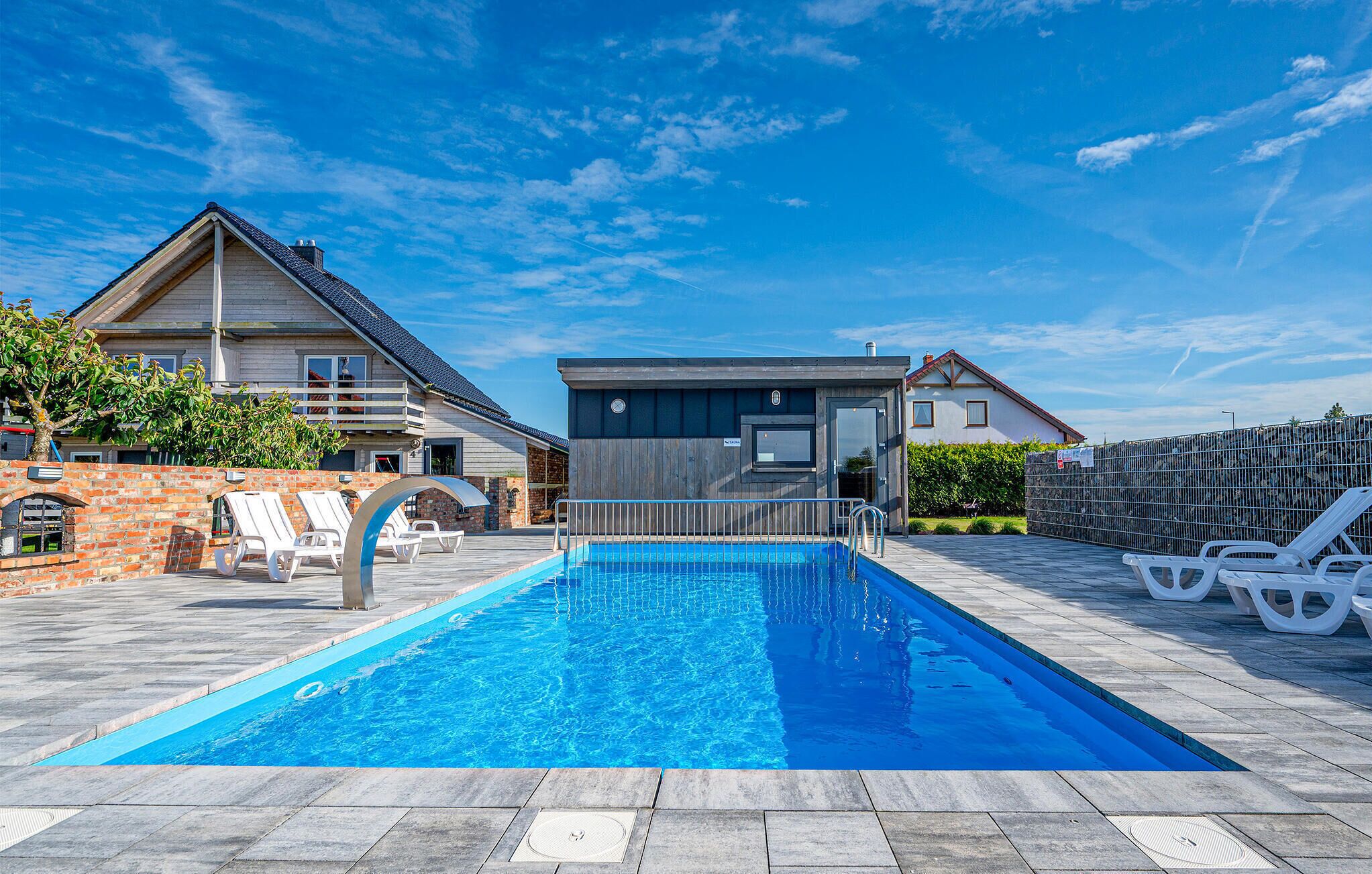 Ein Schwimmbecken mit Liegestühlen, einer Ziegelmauer und zwei Häusern im Hintergrund.
