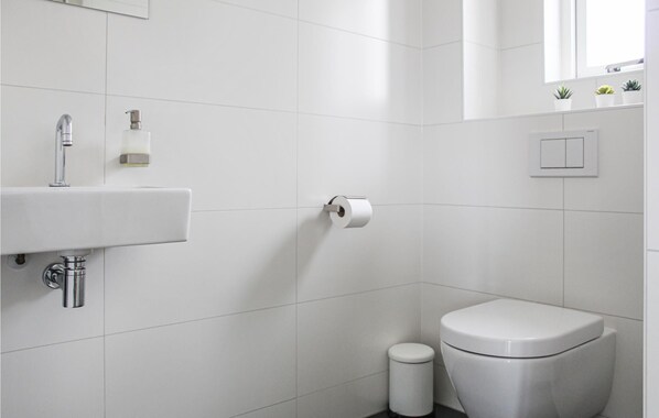 Un baño moderno con un lavabo blanco, inodoro y un dispensador de papel higiénico en la pared.
