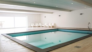 An indoor swimming pool with a tiled floor and walls, white lounge chairs, and a large window providing natural light. - Amazing home in Noordwijk aan Zee (Noordwijk aan Zee)
