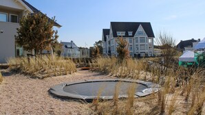 A residential area with a large house, a swimming pool, and a trampoline in a sandy area with sparse vegetation. - Amazing home in Noordwijk aan Zee (Noordwijk aan Zee)