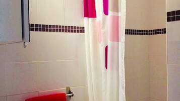 Un baño con un lavamanos blanco, una toalla roja y una cortina de ducha con motivos rosa y blanco.