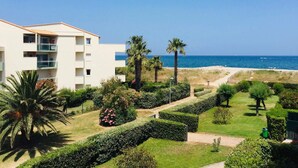 A coastal hotel with a view of the sea, featuring a modern building, manicured gardens, and palm trees.