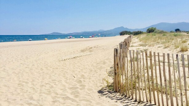 A sandy beach with a wooden fence, clear blue sky, and distant mountains.