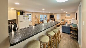 A modern kitchen with a granite countertop, bar stools, and a dining area with a sofa and chairs.