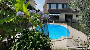 A swimming pool surrounded by lush greenery, with a house in the background. - Rent House Puyôo 8 people (Puyoo)