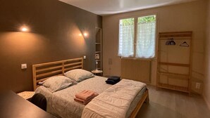 A bedroom with a bed, bedside table, lamp, wardrobe, and a window with curtains. - Rent House Puyôo 8 people (Puyoo)