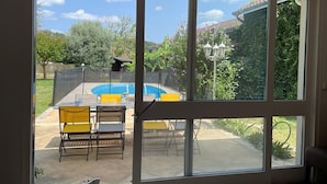 A room with large windows overlooking a backyard with a pool, chairs, and a table. - Rent House Puyôo 8 people (Puyoo)