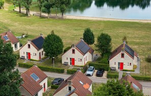 Zona residencial con casas que tienen puertas rojas y paneles solares, rodeada de vegetación y una masa de agua.